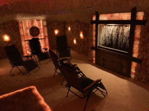 A cozy salt room with reclining chairs, illuminated salt walls, and a calming water feature.