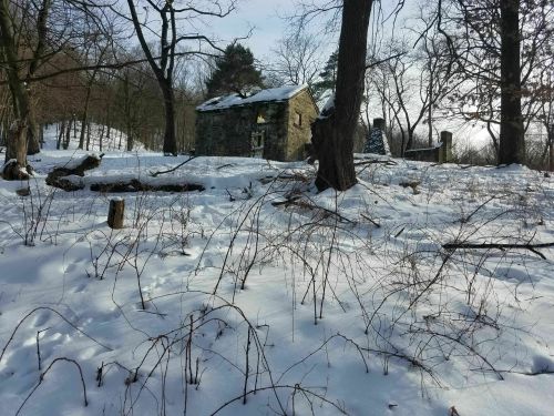 A snow-covered landscape featuring a dilapidated stone building surrounded by bare trees.