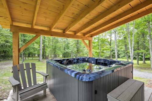 A hot tub under a wooden gazebo, surrounded by trees and a grassy area, with a wooden chair nearby.