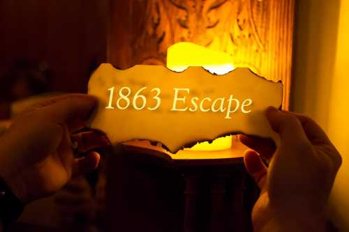 A person holds a burnt-edge sign reading "1863 Escape" near a glowing candle.