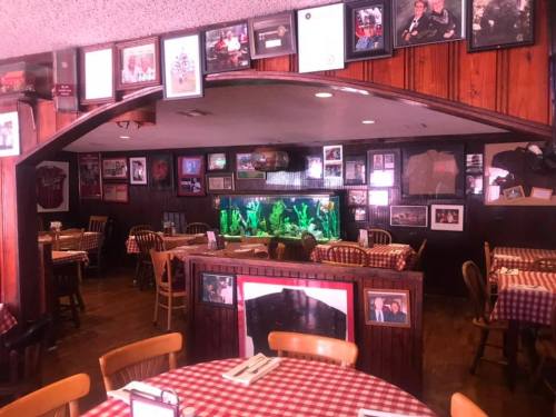 Cozy restaurant interior with checkered tablecloths, wooden chairs, and walls adorned with framed photos and an aquarium.