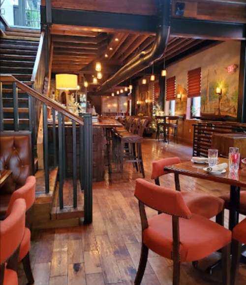 Cozy restaurant interior with wooden floors, warm lighting, and a staircase leading to an upper level.