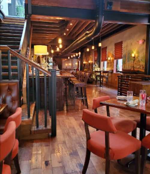 Cozy restaurant interior with wooden floors, warm lighting, and a staircase leading to an upper level.