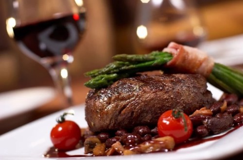 A gourmet steak served with asparagus, cherry tomatoes, and a red wine reduction on a white plate.