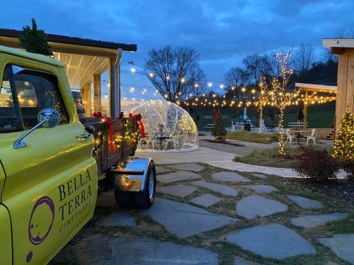 A yellow truck parked near a cozy outdoor dining area with string lights and a transparent dome, set against a twilight sky.