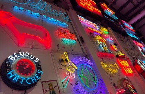 A vibrant display of vintage neon signs in various colors and designs, illuminating a wall.