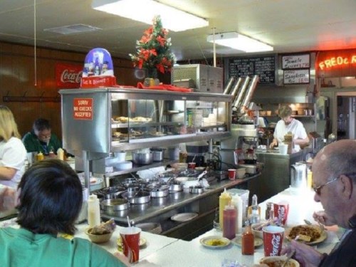 A busy diner kitchen with patrons enjoying meals at the counter, surrounded by cooking equipment and condiments.