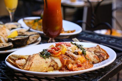A delicious omelette topped with sauce, cheese, and vegetables, served on a white plate with drinks in the background.