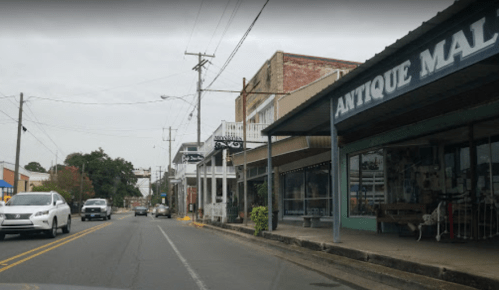 A street view of a small town featuring shops, including an antique mall, under a cloudy sky.