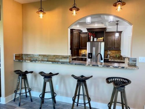 A modern kitchen bar with four metal stools, stone accents, and pendant lighting above a granite countertop.