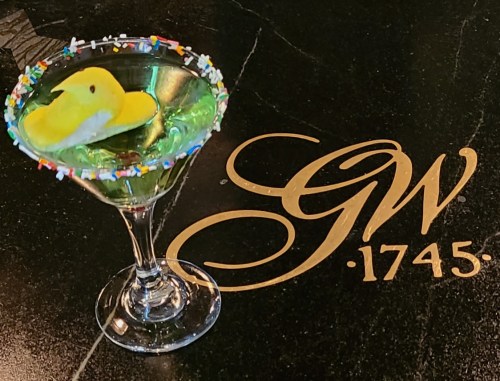 A colorful cocktail with a marshmallow chick and sprinkles, placed on a black surface with "GW 1745" engraved.