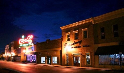 A quiet street at night featuring vintage storefronts and colorful neon signs.