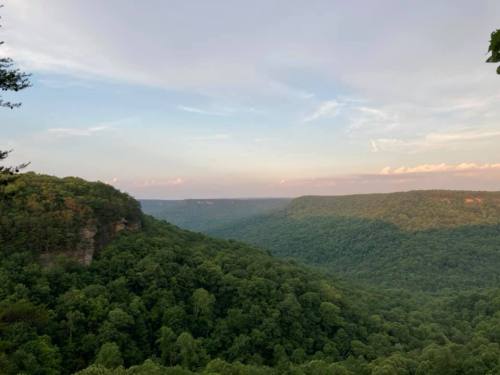 A scenic view of lush green hills and valleys under a soft, cloudy sky at dusk.
