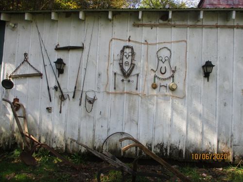 A rustic white wall displays various tools and metal art, including lanterns, fishing rods, and decorative figures.