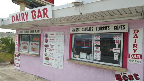 A colorful dairy bar with a menu featuring shakes, sundaes, flurries, and cones, with an "Open" sign.