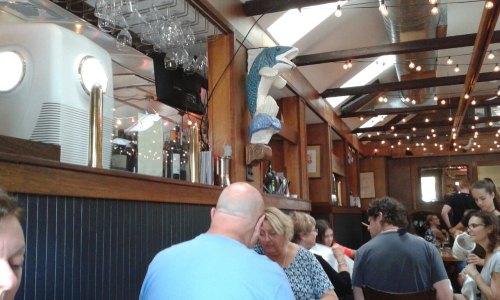A bustling restaurant interior with wooden beams, string lights, and a decorative fish mounted on the wall.