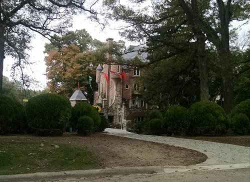 A stone castle-like building surrounded by trees and manicured bushes, with flags flying from its towers.