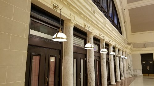 Interior view of a hallway with marble columns and vintage light fixtures hanging from the ceiling.