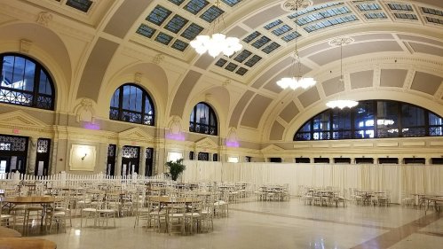 A spacious, elegantly designed hall with high ceilings, large windows, and tables set for an event.
