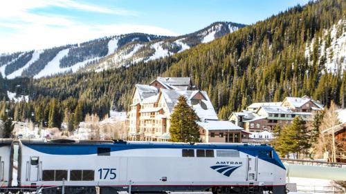 Amtrak train 175 in front of a snowy mountain landscape and a lodge surrounded by evergreen trees.