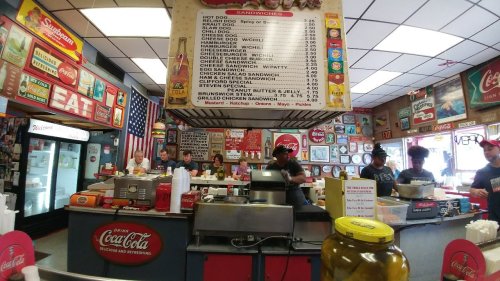A bustling diner with a menu board, vintage decor, and staff serving customers at the counter.