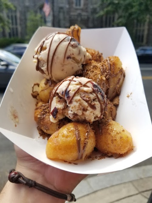 A hand holding a tray of warm dough balls topped with ice cream and drizzled with chocolate sauce.