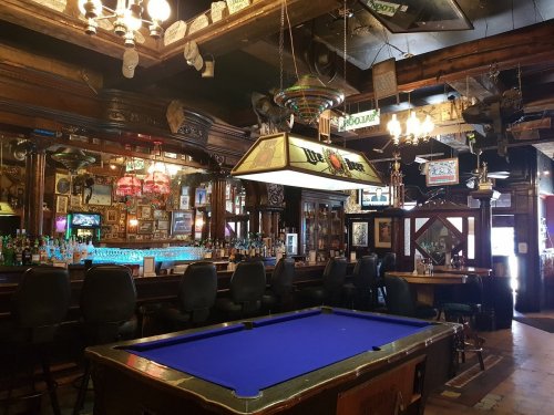 A cozy bar interior featuring a blue pool table, wooden decor, and a well-stocked bar with vintage lighting.