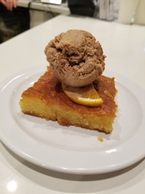 A slice of yellow cake topped with a scoop of chocolate ice cream and a slice of orange on a white plate.