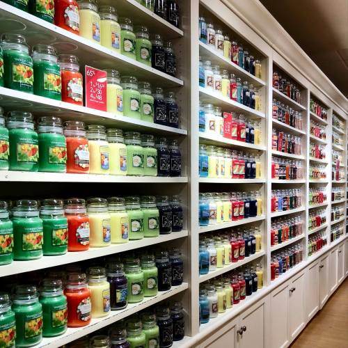A wall of colorful candles in jars, neatly arranged on shelves in a well-lit store.
