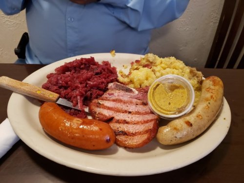 A plate of assorted meats including sausage, sliced ham, and corned beef, served with mustard and a side of mashed potatoes.