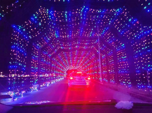 A colorful tunnel of lights in blue and purple, viewed from a car at night, creating a festive atmosphere.