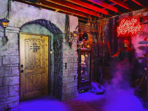 A spooky room with a stone door, eerie decorations, and a glowing "Camp of Horror" sign, shrouded in fog.