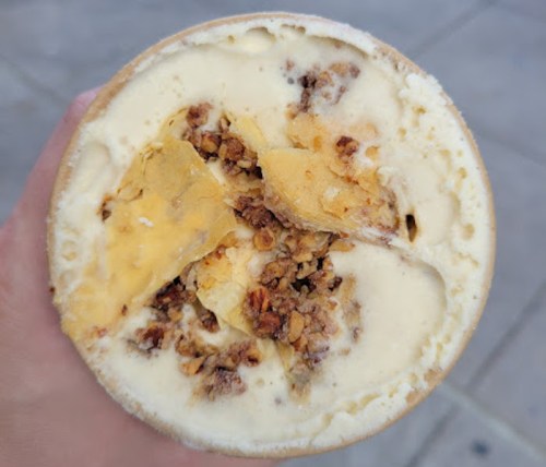 A close-up of a cup of ice cream with granola and chunks of caramel or toffee mixed in.