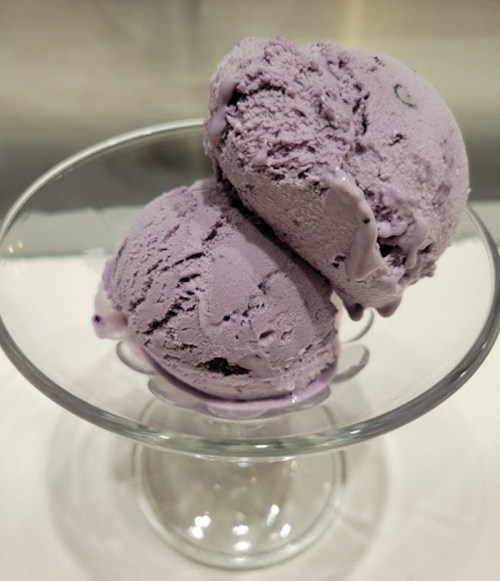 Two scoops of purple ice cream in a clear glass dish.