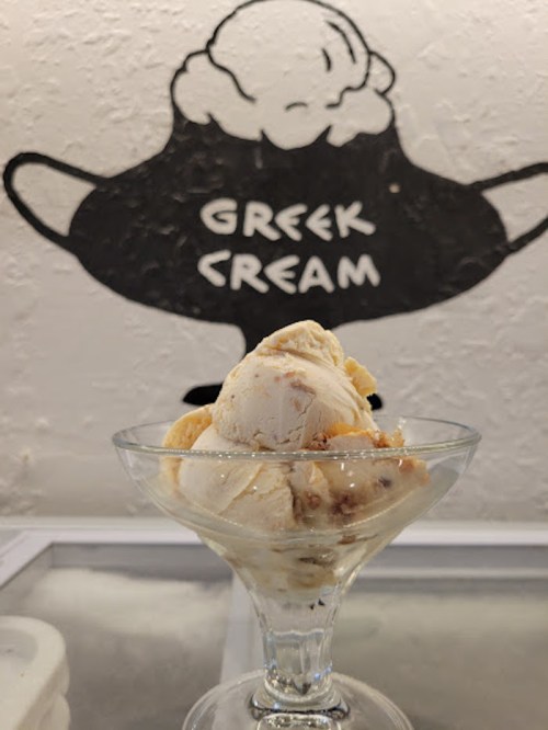 A glass dish of ice cream sits in front of a wall mural that reads "Greek Cream."