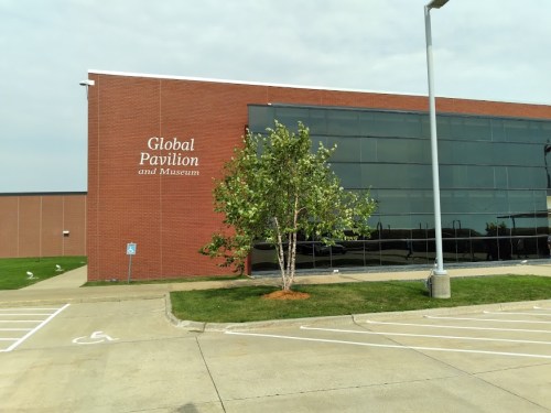 Exterior view of the Global Pavilion and Museum building, featuring a tree and parking area in front.