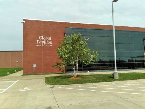 Exterior view of the Global Pavilion and Museum building, featuring a tree and parking area in front.