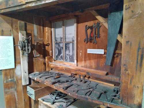 A wooden workshop display featuring various tools, a window, and a saw against a rustic wall.