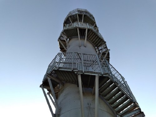 A tall, cylindrical structure with a spiral staircase and metal railings against a clear sky.