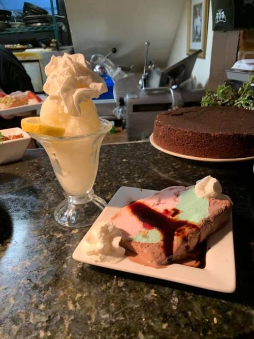A dessert plate featuring a slice of mint chocolate ice cream with whipped cream and a glass of lemon sorbet.