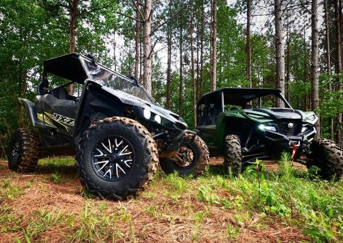 Two off-road vehicles parked in a forested area, surrounded by trees and greenery.
