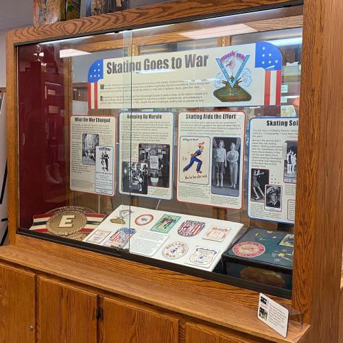Display case featuring a "Skating Goes to War" exhibit with historical photos and artifacts related to skating during wartime.