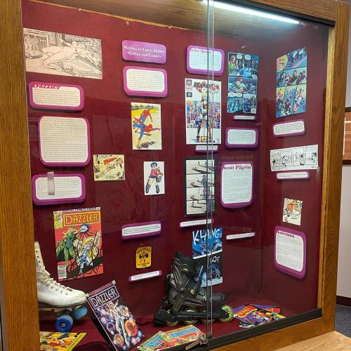 Display case featuring vintage comics, roller skates, and informational panels about pop culture and history.
