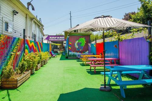 Colorful outdoor space with vibrant murals, picnic tables, and greenery under a clear blue sky.