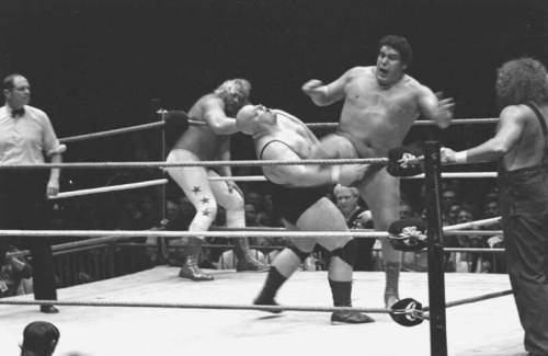 A black-and-white wrestling match featuring two wrestlers in action, with a referee and another wrestler in the background.
