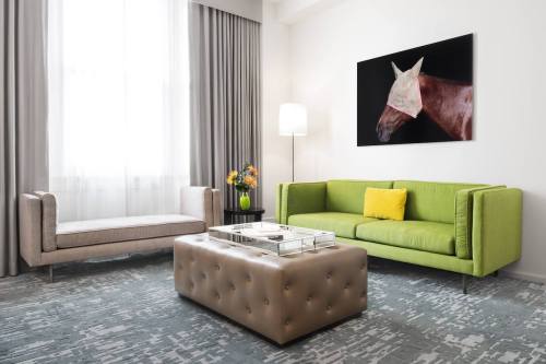 Modern living room featuring a green sofa, beige loveseat, coffee table, and a horse painting on the wall.