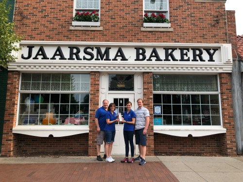 Four people stand in front of Jaarsma Bakery, a brick building with large windows and a sign above.
