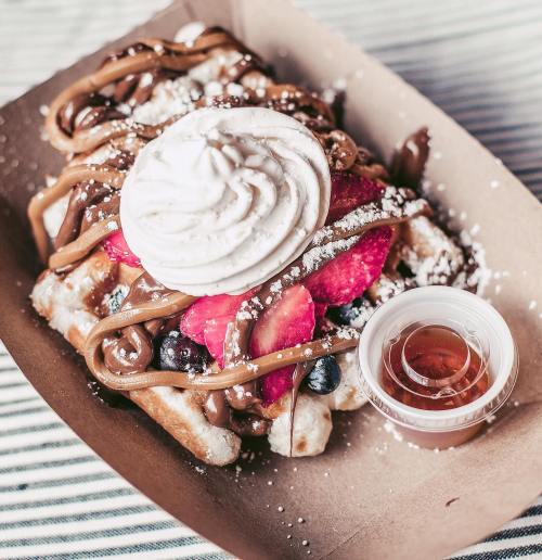 A delicious waffle topped with whipped cream, strawberries, blueberries, and drizzled with chocolate sauce, served with syrup.