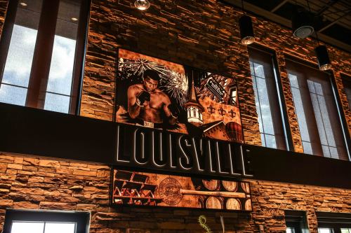 A vibrant mural featuring a muscular figure and elements representing Louisville, with stone walls and large windows.