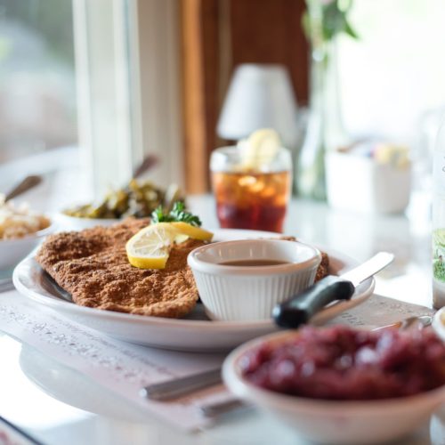 A plate of fried fish with lemon, dipping sauce, and sides of greens and coleslaw on a table with a drink.